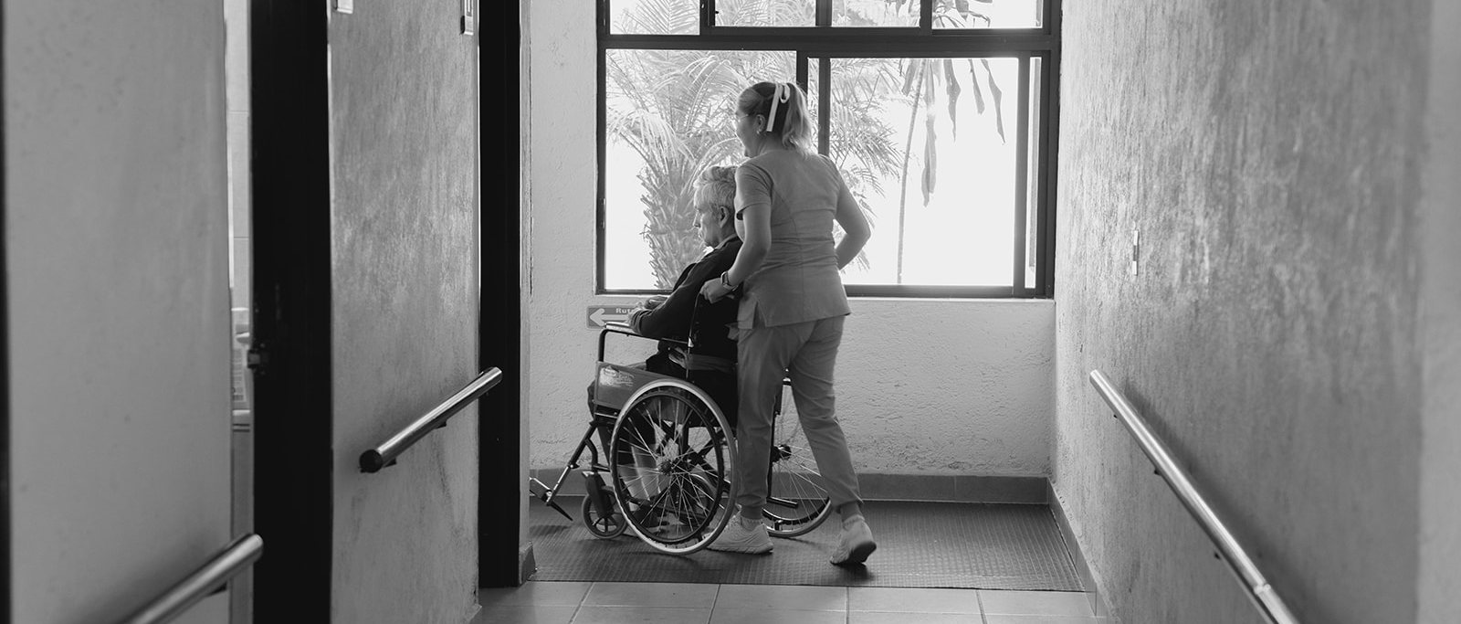 Cuidadora acompañando a un residente en silla de ruedas por un pasillo